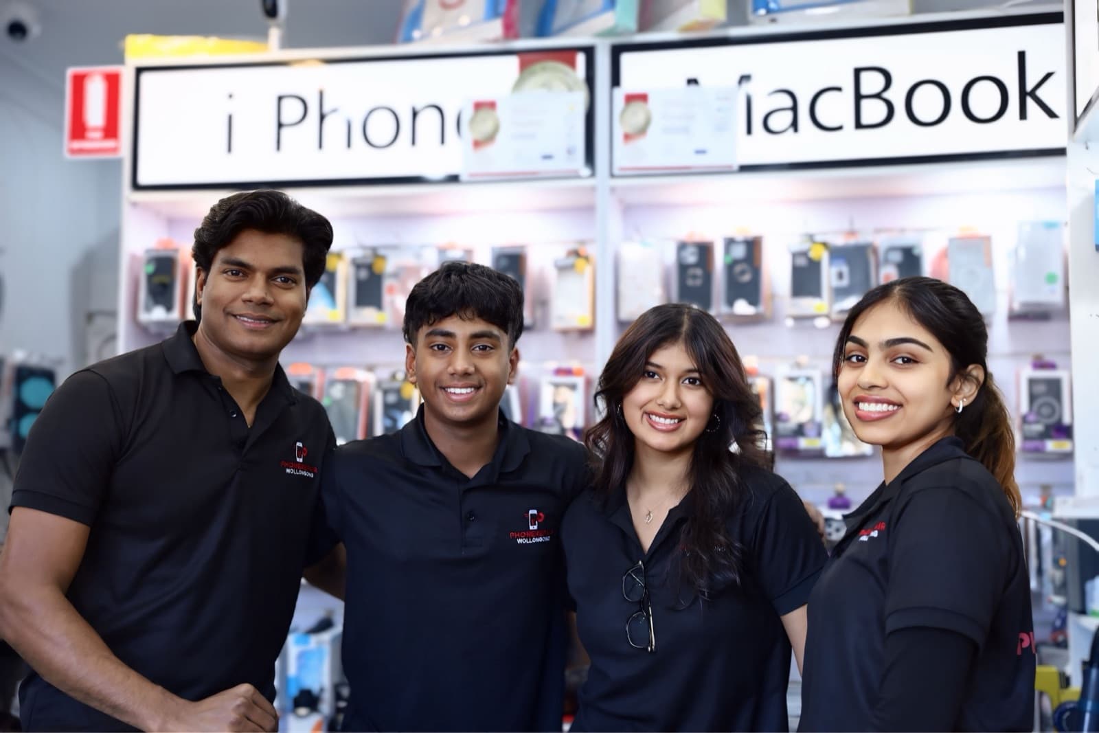 Four members of the Phone Repair Wollongong team smiling inside the shop, under the iPhone and MacBook repair signs.